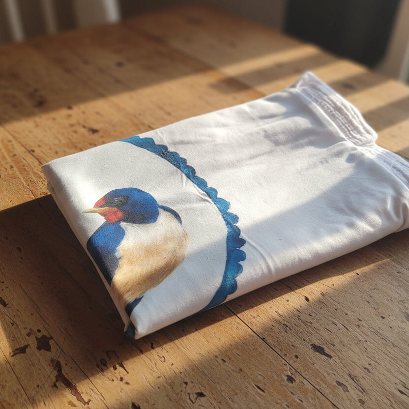 White baby blanket with a blue and red bird design on a beige bed.