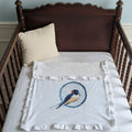 Wooden crib with a white blanket featuring a blue bird design on a light blue wall.